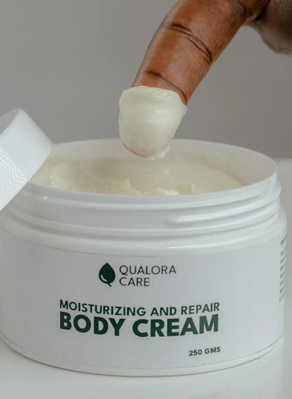 A fingertip lifting rich, creamy Qualora Care Body Cream from an open 250 g jar