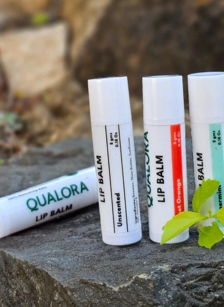 Qualora Care Lip Balm tubes in Unscented, Sweet orange and Peppermint on a natural stone with a fresh green leaf